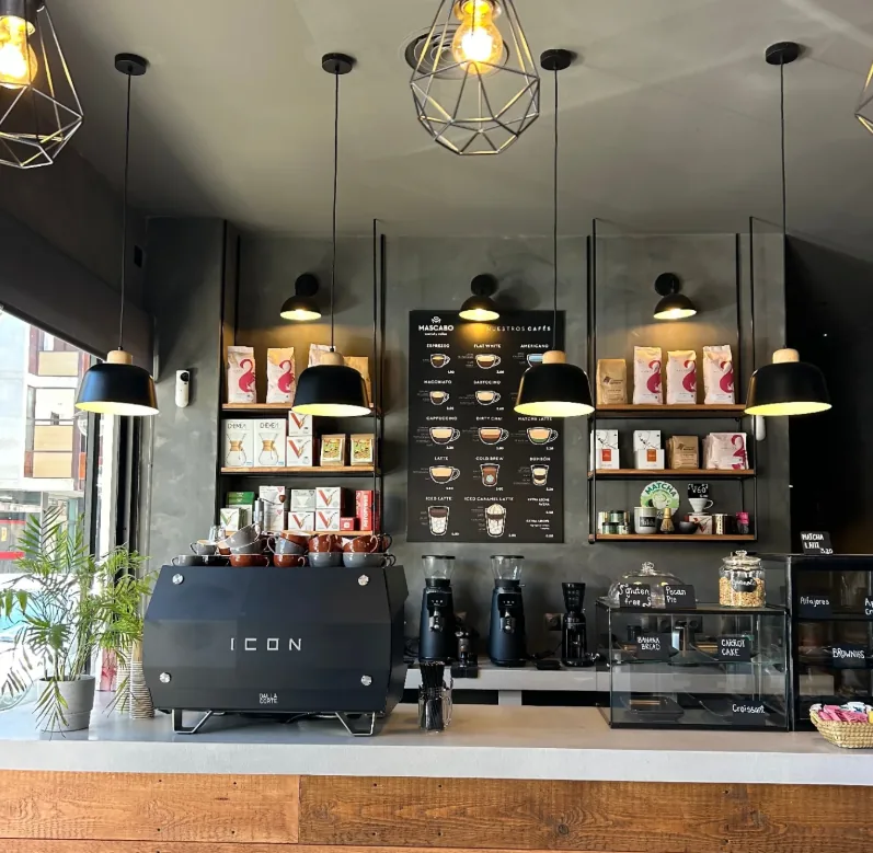 Barra interior de Mascabo con la máquina de espresso, la vitrina de pastelería y las lámparas colgantes
