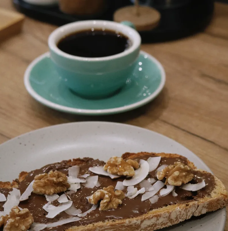 Tostada con crema de chocolate, coco laminado y nueces junto a un café solo